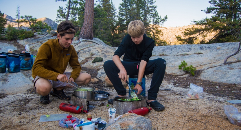 two outward bound students work to prepare food among rocks and tress
